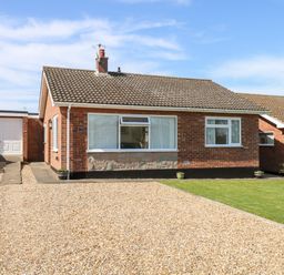 A single-story brick house with a tiled roof a gravel driveway and a small lawn at Elliotts Retreat in Sheringham