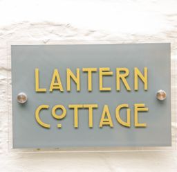 A sign with yellow letters saying Lantern Cottage mounted on a white textured wall at Lantern Cottage in Padstow