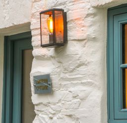 An exterior wall with a lit lantern and a sign reading Lantern Cottage next to blue framed windows at Lantern Cottage in Padstow
