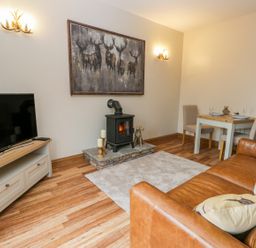 A living room with a brown leather sofa a stove with candles a dining table with two chairs and a television on a stand at Wagtail Nest Northfield Cottage in Scalby