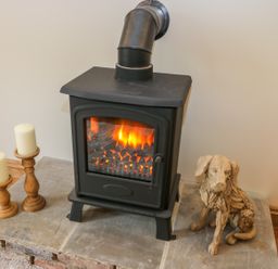 A black wood stove with fire inside next to two white candles on wooden holders and a wooden dog sculpture at Wagtail Nest Northfield Cottage Scalby