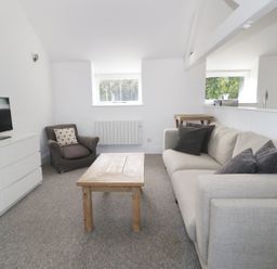 A living room with a gray armchair beige sofa wooden coffee table white dresser with television at Orchard Cottage in Shaftesbury