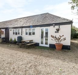 The exterior of a single story cottage with windows a door a picnic bench plant pots and a gravel driveway at Orchard Cottage in Shaftesbury