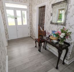 An entryway with a white door a table with flowers and cards a chair and a mirror at Kates Cottage near Ballina County Mayo