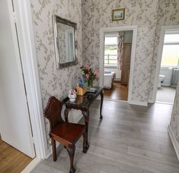 A hallway with a wooden chair and table with flowers and brochures a mirror on the wall and doorways leading to a bedroom and a bathroom at Kates Cottage near Ballina County Mayo