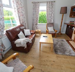 A living room with a brown leather sofa two patterned armchairs wooden coffee table lamp fireplace and floral curtains at Kates Cottage near Ballina County Mayo