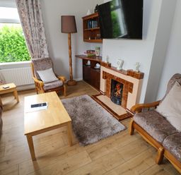 A living room with wooden furniture a fireplace a television and a window with curtains at Kates Cottage near Ballina County Mayo