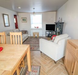 A living room with wooden dining table and chairs a beige sofa armchair fireplace and television at Cranny Corner in Carnlough