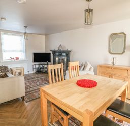 A living room with a wooden dining table and chairs a sofa a television an ornate fireplace a sideboard with a lamp and mirror at Cranny Corner in Carnlough