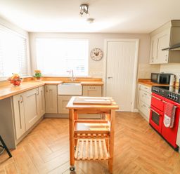 A kitchen with wooden countertops a red oven a movable wooden island and a wall clock at Cranny Corner in Carnlough