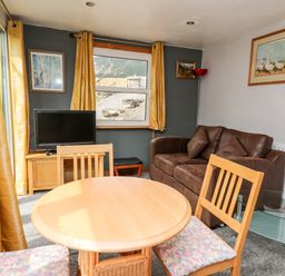 A dining area with round wooden table and chairs a brown sofa a TV on a wooden stand and paintings on walls at The Hen Pen in Star near Cenarth