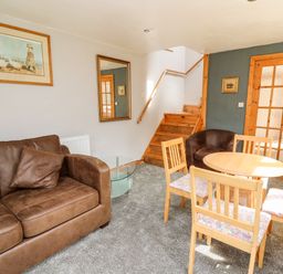 A living room with a brown sofa a round wooden dining table with four chairs a staircase a framed picture and a mirror on the wall at The Hen Pen in Star near Cenarth