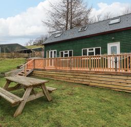 A green wooden house with a deck and picnic table on a grass lawn at The Hen Pen in Star near Cenarth