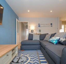 A living room with a blue sofa patterned cushions a rug with an anchor a wooden coffee table and oars on the wall at Coastal Haven Crackington near Crackington Haven