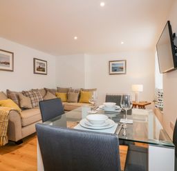 A dining area with a glass table set for four and a seating area with a sofa and cushions at Midships in Mevagissey