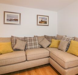 An L-shaped beige sofa with multiple cushions and two framed pictures on the wall at Midships in Mevagissey