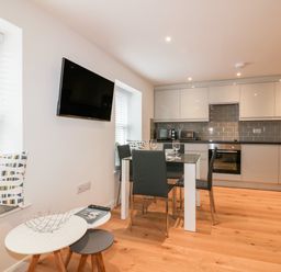 A kitchen with white cabinets a dining table with four chairs and a wall mounted TV at Midships in Mevagissey