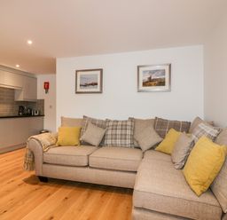 A beige sofa with yellow and plaid cushions in a living area next to a modern kitchen at Midships in Mevagissey