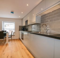 A kitchen with white cabinets black countertop gray tile backsplash and a dining table with chairs at The Crows Nest in Mevagissey