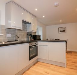 A kitchen with white cabinets gray backsplash and wooden floor at Captain's Cabin in Mevagissey