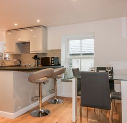 A kitchen with a counter and two bar stools next to a dining table with four chairs and a window at Captains Cabin in Mevagissey