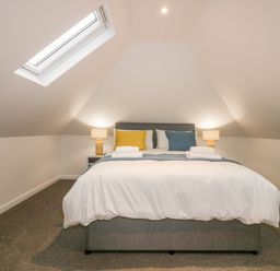 A bedroom with a bed two bedside tables two lamps and skylight windows at Captain's Cabin in Mevagissey