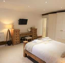 A bedroom with a wooden bed, white wardrobes, a wooden desk with drawers, a black armchair, a lamp, and a wall-mounted TV at The Penthouse Lynmouth Bay in Lynton
