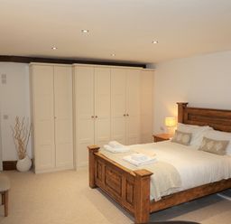 A bedroom with a wooden bed frame bedside tables lamps and cream wardrobes at The Penthouse Lynmouth Bay in Lynton