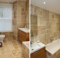 A bathroom with beige tiled walls and floor featuring a toilet, a wooden vanity with sink, a bathtub with shower and glass screen at The Penthouse Lynmouth Bay in Lynton