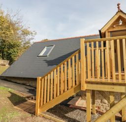 A wooden staircase leading to an elevated porch with a door on a building with a slate roof and a skylight at The Lookout in Llangrove