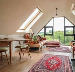 An attic living room with skylights a wooden table with chairs a brown sofa cushions a television and patterned rugs at The Lookout in Llangrove