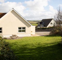 A garden area with grass and a wooden picnic table beside a cream colored house at Bramble Cottage in Newgale