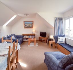A living room with blue sofas a wooden coffee table a dining table with chairs and a window seat at Bramble Cottage in Newgale