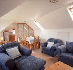 A living room with blue armchairs dining table with chairs and kitchen in the background at Bramble Cottage in Newgale