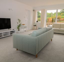 A living room with a green sofa a white sofa a large television and windows showing a garden at Thames Reach in Wallingford