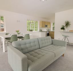 An open plan room with a sofa dining table with chairs kitchen appliances and bar stools at Thames Reach in Wallingford