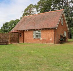 A brick house with a pitched roof in a grassy yard with a wooden bench a small table with two chairs and a barbecue grill at Thames Reach in Wallingford