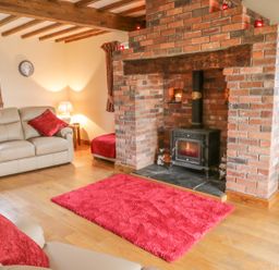 A living room with a brick fireplace leather sofas and red cushions at Ty Berllan in Caersws