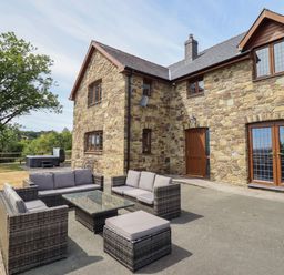 An outdoor seating area with a stone house and hot tub at Ty Berllan Caersws