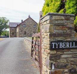 A stone house with a driveway and gate at Ty Berllan in Caersws