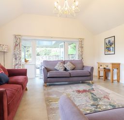A living room with sofas a rug a wooden desk and a wall-mounted television at Ochr Y Garth in Maenan