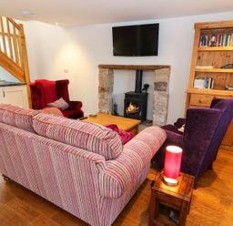 A living room with a striped sofa two armchairs a fireplace a wooden bookcase and a small table lamp at Linden Cottage in Ravenstonedale Nr Kirby Stephen