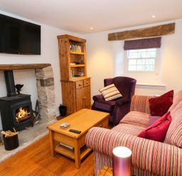 A living room with a wood burning stove under a stone fireplace and a wall mounted tv at Linden Cottage in Ravenstonedale Nr Kirby Stephen