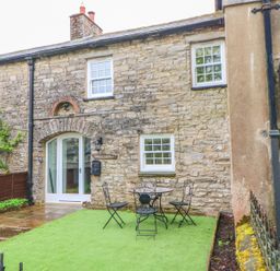 A stone cottage exterior with white framed windows and a small table with three chairs on a grass area at Linden Cottage Ravenstonedale Nr Kirby Stephen