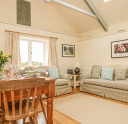 A living room with a wooden dining table set with plates and glasses and plaid sofas with cushions at Oreos Cottage in St Agnes