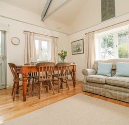 A dining area with a wooden table and chairs next to a plaid sofa with cushions at Oreo's Cottage in St Agnes