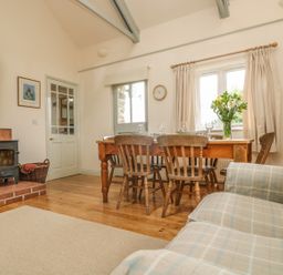A dining area with a wooden table and chairs a wood burning stove and a sofa at Oreos Cottage in St Agnes