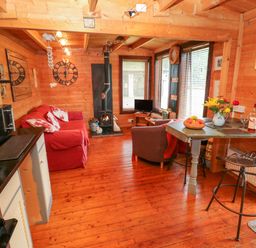 A cabin living area with red sofa a wood stove a small dining table and kitchen appliances at The Lodge in Rosemarket