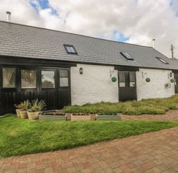 A row of white stucco cottages with black doors and windows and flower pots on a brick pathway at Heather Cottage in Rosemarket