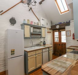 A kitchen with wooden countertops cupboards a refrigerator a sink and wooden double doors at Heather Cottage in Rosemarket